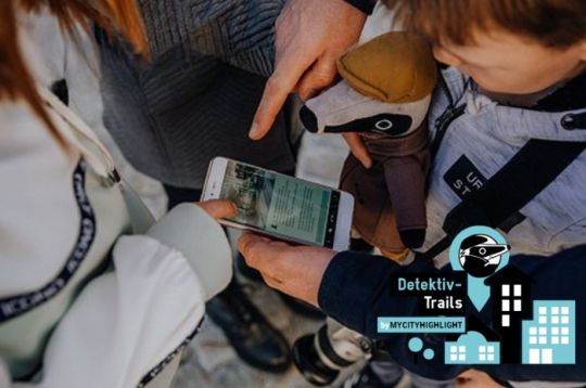 Personen inspizieren ein Smartphone-Display, während ein Kind ein Kuscheltier hält. Umgebung im Freien.