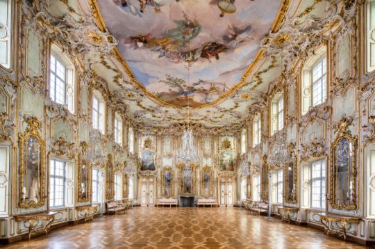 Eleganter barocker Saal mit kunstvollen Dekorationen, Kronleuchtern und gemalter Decke.