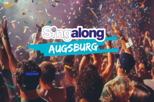 Eine lebhafte Menschenmenge bei einem Konzert mit Konfetti, Lichtern und dem Text 'Singalong Augsburg' in fetten Buchstaben.