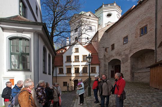 Eine Gruppe auf einer Tour erkundet eine historische Straße mit alten Gebäuden unter blauem Himmel.