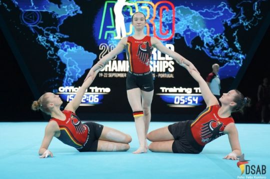 Drei Turnerinnen in passenden Uniformen führen eine synchronisierte Routine bei einer Meisterschaft auf.