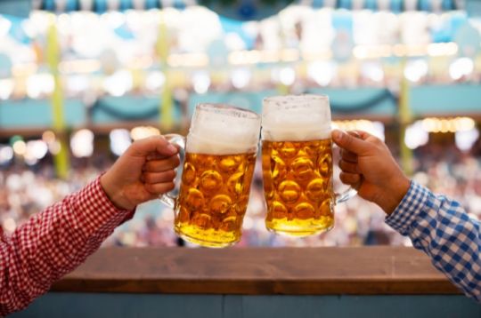Zwei Personen stoßen mit Bierkrügen auf einer festlichen Veranstaltung an.