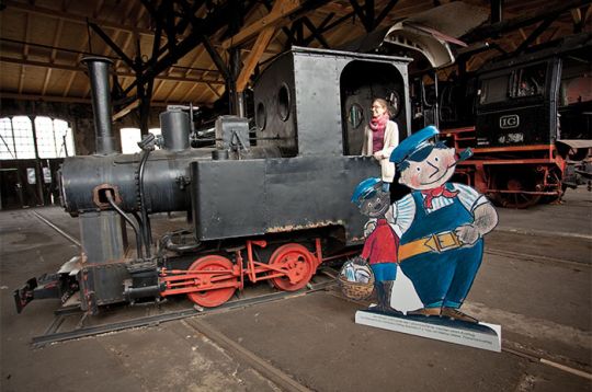 Eine kleine Dampflokomotive in einem historischen Lokschuppen mit Pappfiguren von Zeichentrickfiguren daneben.
