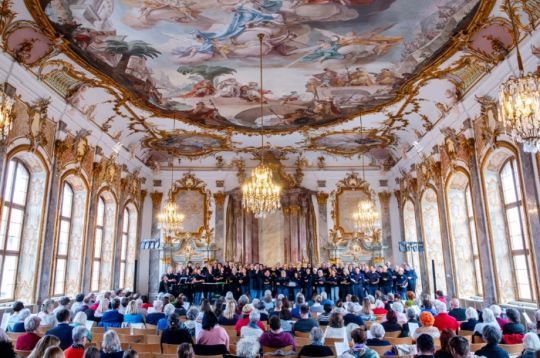 Chor singt in einem prächtigen, mit vielen Zuschauern gefüllten Saal.