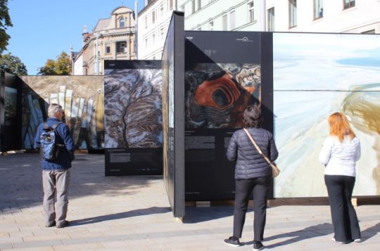 Besucher betrachten großformatige Fotografien von Landschaften auf einer Außenausstellung auf dem Augsburger Königsplatz.