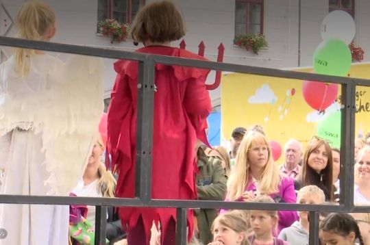 Kinder in Kostümen, eines als Engel und eines als Teufel, treten auf einer Bühne vor Publikum auf.