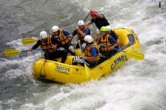 Eine Gruppe Menschen beim Wildwasser-Rafting in einem gelben Boot mit Sicherheitsausrüstung auf einem turbulenten Fluss.