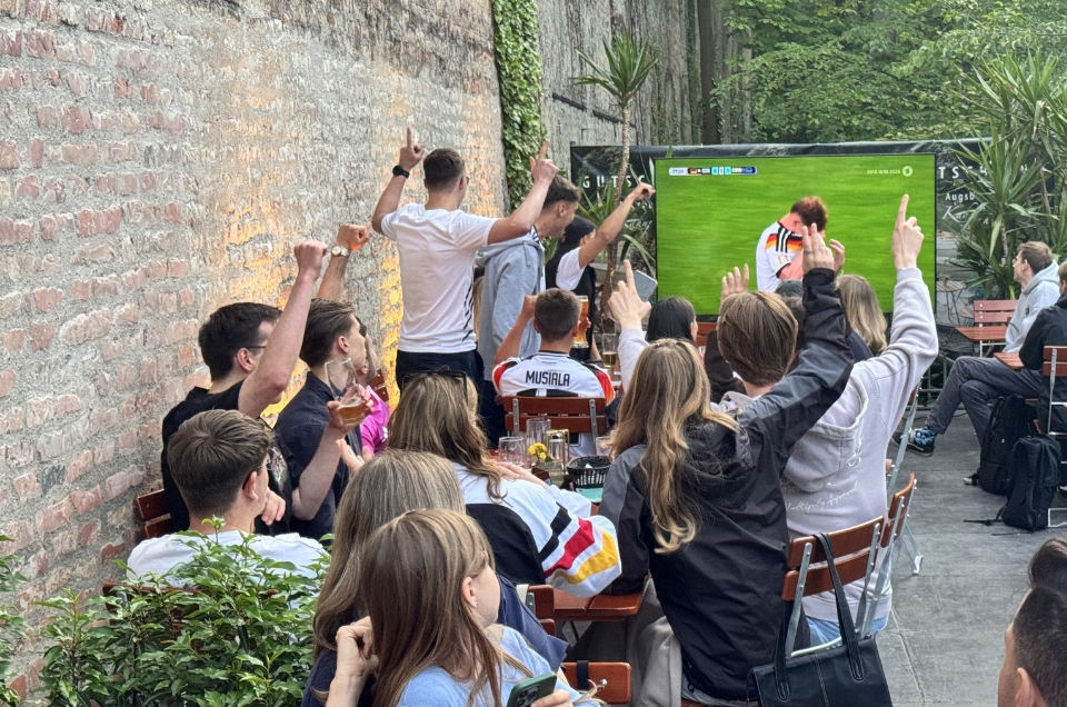 Eine lebhafte Gruppe von Menschen, die ein Fußballspiel auf einem Außenschirm leidenschaftlich bejubeln.