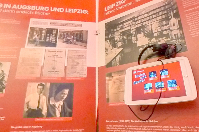 Ausstellungsdisplay mit historischen Bildern und Dokumenten über Bücher in Augsburg und Leipzig. Enthält ein Tablet mit Kopfhörer.