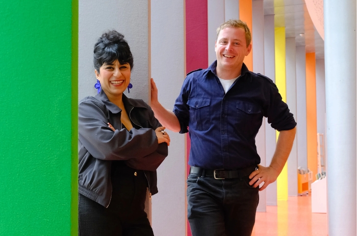Zwei lächelnde Personen in einem bunten Flur mit modernen Designelementen.