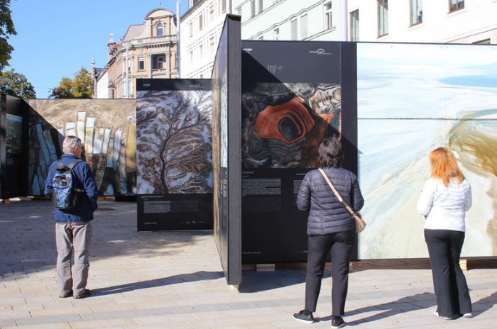 Besucher betrachten großformatige Fotografien von Landschaften auf einer Außenausstellung auf dem Augsburger Königsplatz.