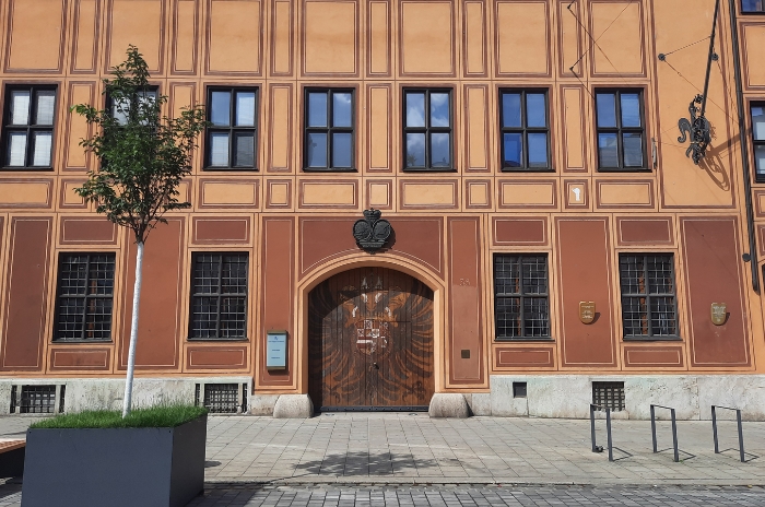 Frontansicht eines historischen Gebäudes mit verzierten Fenstern und einer großen Holztür.