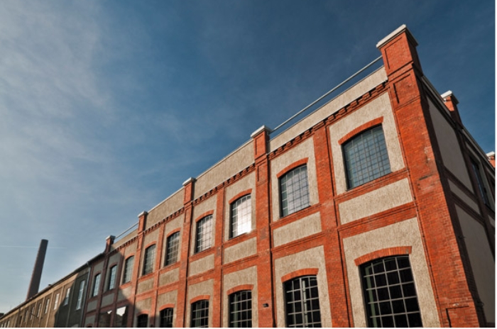 Historisches Backsteingebäude mit großen Fenstern vor klarem blauen Himmel.