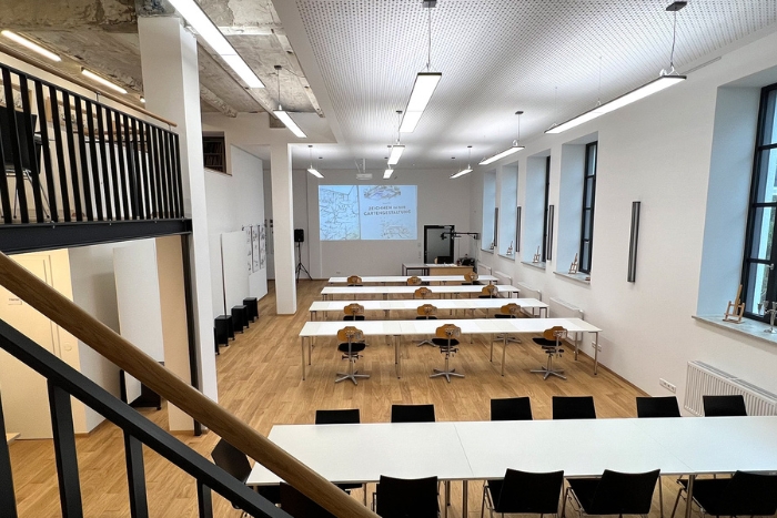Moderner Seminarraum mit weißem Interieur, Projektor und Tischen in Reihen aufgestellt.